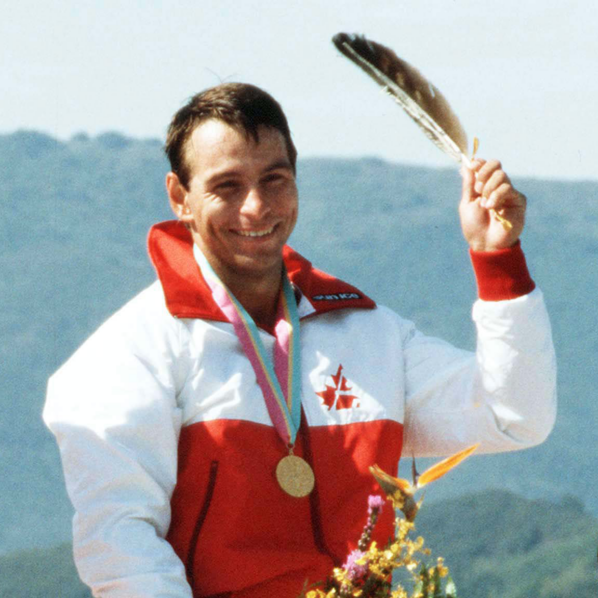 Alwyn Morris, on a podium having won Gold at the Olympics, poses with an eagle feather